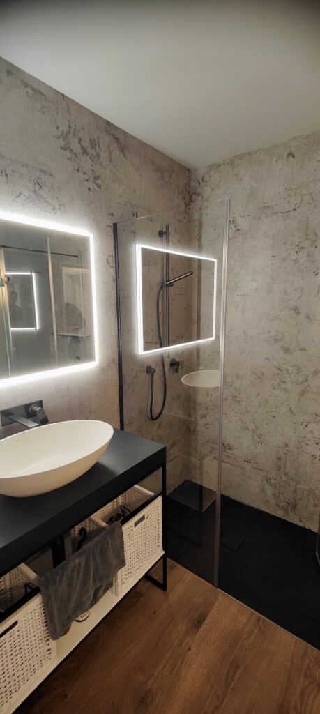 Individuelles Badezimmer mit Tapete in der Dusche und schwarzen Armaturen
